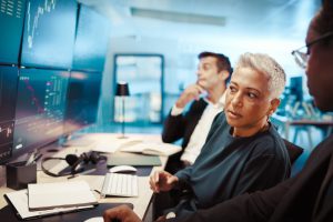 Computer screen, trading and business people in office, advice and internet with economy graphs. Em.